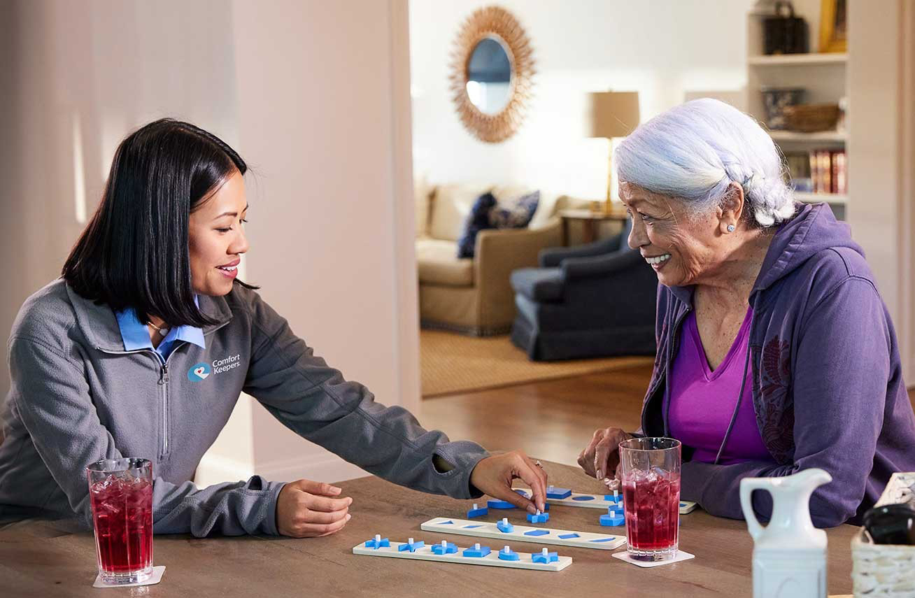 cuidadora jogando com mulher idoso numa sala de casa