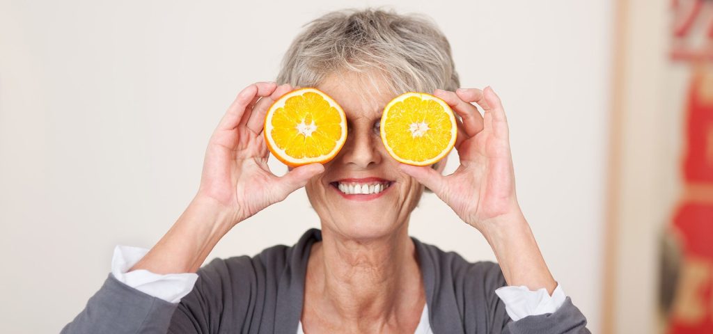Mulher idoso de frente com duas metades de uma laranja em cada olho